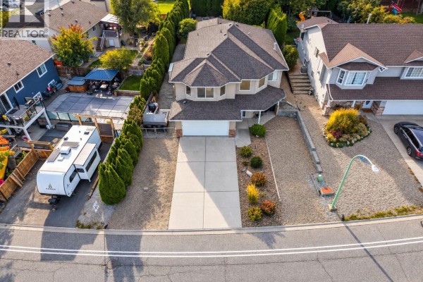 Aerial view of a beige house with a driveway, garage, and surrounding homes. - 1380 Loseth Drive, Kelowna