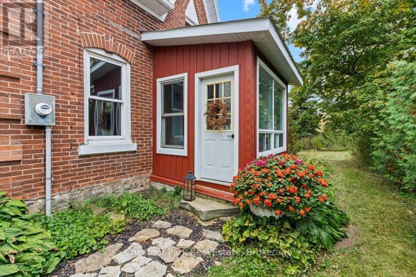 Red-paneled porch with a white door, stone pathway, and potted flowers. - 138237 Grey Road 112, Meaford