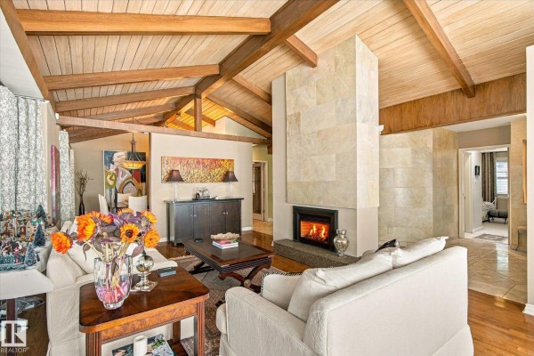 Living room with vaulted wood-beamed ceiling, stone fireplace, and white sofas. - 13862 Ravine Dr Nw, Edmonton