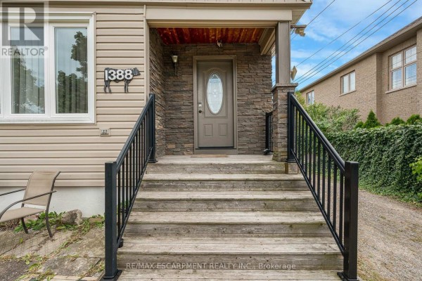 Close-up of the front door with stone accents, wooden steps, and black metal railings. - 1388/1390 Leighland Road, Burlington