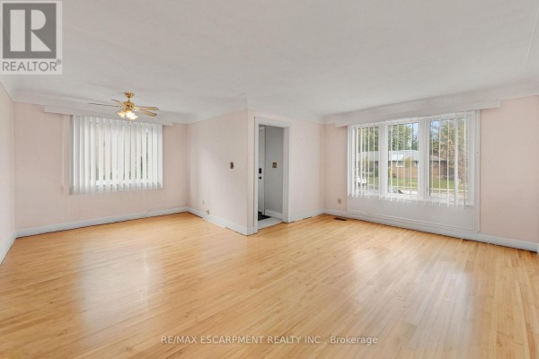 Spacious living room with hardwood floors, light pink walls, and large windows overlooking the front yard. - 1388/1390 Leighland Road, Burlington