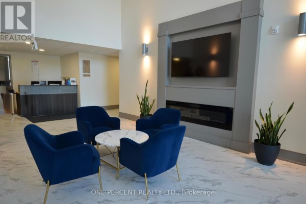 Apartment building lobby with four navy blue chairs, a marble coffee table, and a modern fireplace. - 139 - 50 Herrick Avenue, St  Catharines