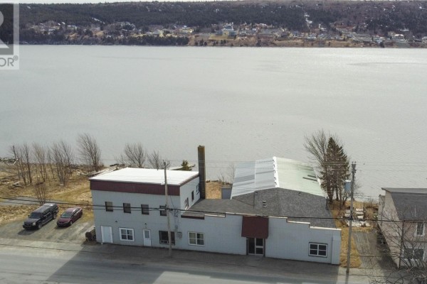 The grey commercial building situated on the waterfront with a wide expanse of water behind it. - 139-141 Water Street, Harbour Grace