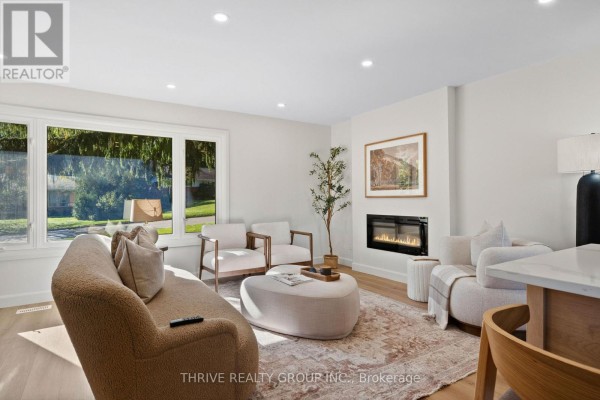 Living room with fireplace, large window, sofa, chairs, and ottoman with light wood floors. - 139 Deer Park Circle, London North