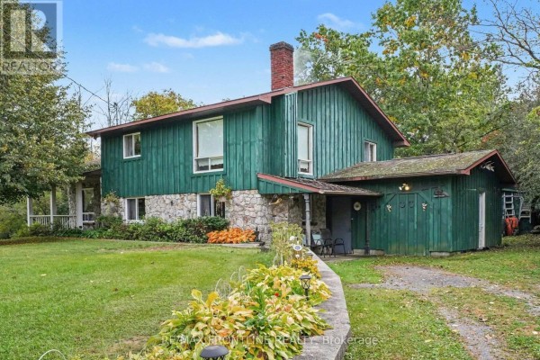 Exterior of a two-story green house with a stone lower level, featuring a covered porch and attached garage. - 139 Port Elmsley Road, Drummond/north Elmsley
