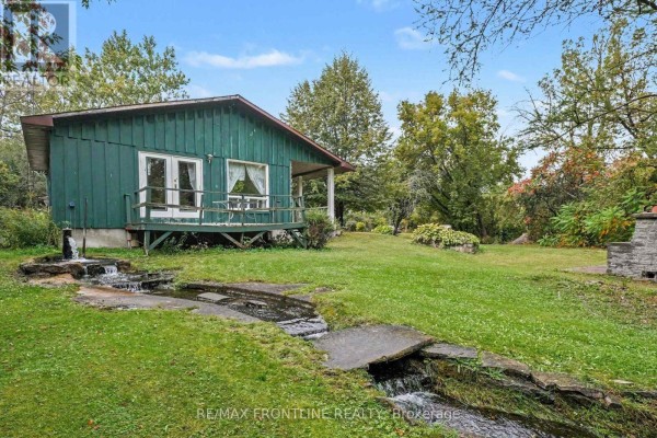 Small green detached structure with a covered porch, facing a grassy yard with a small man-made stream. - 139 Port Elmsley Road, Drummond/north Elmsley