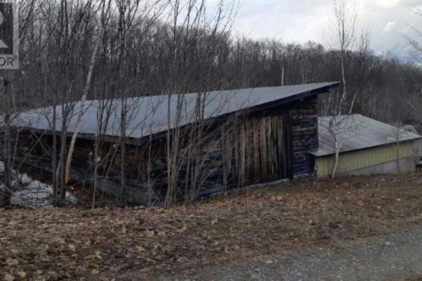 Rustic log cabin structure with a sloped metal roof, surrounded by bare trees. - 1390 Goulais Ave, Sault Ste  Marie