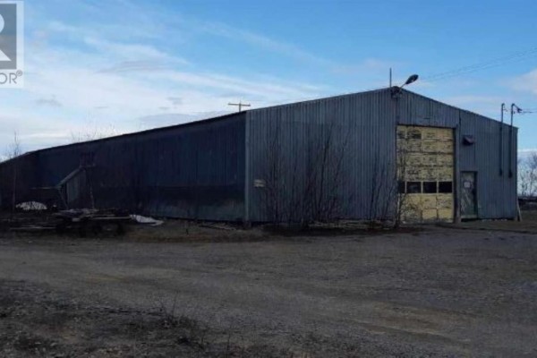 Long view of a large metal warehouse building with multiple loading doors and a gravel lot. - 1390 Goulais Ave, Sault Ste  Marie