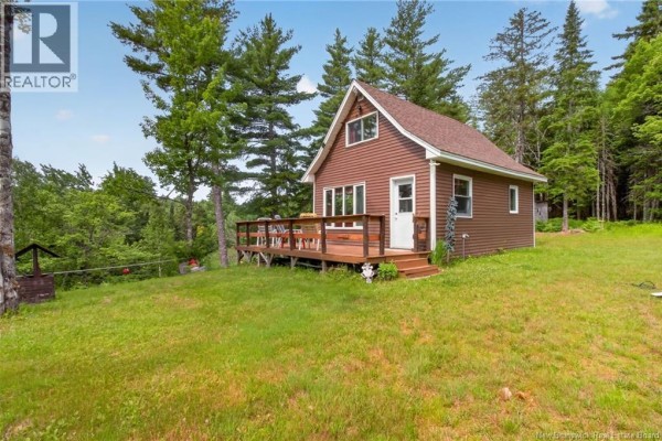 Exterior of a small, brown wooden cabin with a large wooden deck, set on a grassy hill. - 1391 Tweedie Brook, Kouchibouguac
