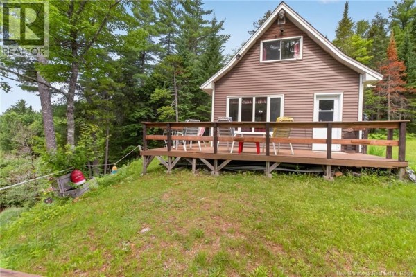Front view of the brown cabin with a wooden deck featuring chairs and tables. A white door is visible. - 1391 Tweedie Brook, Kouchibouguac