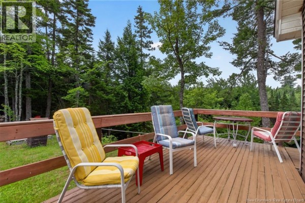 Close-up of colorful striped lounge chairs and small tables on a wooden deck overlooking a wooded area. - 1391 Tweedie Brook, Kouchibouguac