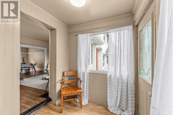 Entryway with a wooden chair, window with white curtains, and door to living room. - 1394 Davenport Road, Toronto