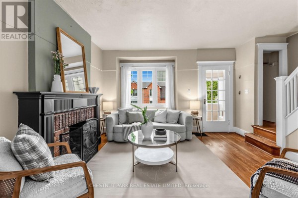 Living room with a black fireplace, grey sofa, glass coffee table, and hardwood floors. - 1394 Davenport Road, Toronto