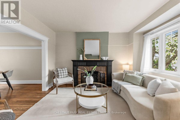 Living room with a fireplace, large window, beige sofa, and armchair, overlooking dining area. - 1394 Davenport Road, Toronto