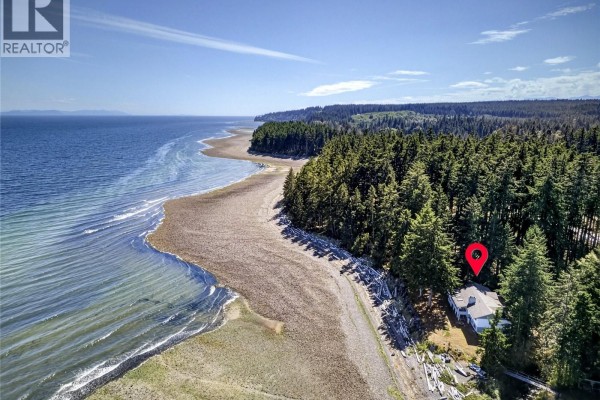 Aerial view of the property nestled amongst trees on a rocky shoreline, with the vast ocean on the left. - 1394 Seaview Rd, Black Creek