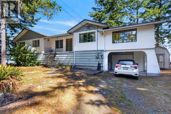 Front exterior of the house with a car parked in an arched carport, adjacent to a small shed. - 1394 Seaview Rd, Black Creek