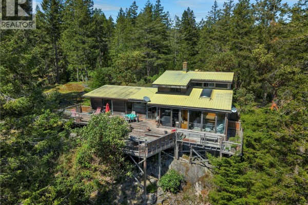 Close-up aerial view of a house with a large wooden deck on a wooded cliffside. - 1395 Manzanita Rd, Cortes Island