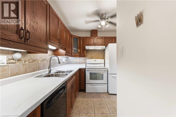 Kitchen with wood cabinets, white countertops, stainless steel sink, and white appliances. - 1396 Upper Ottawa Street Unit# 27, Hamilton