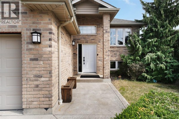 Close-up front entrance of a brick house with a white door, concrete path, and wooden bench. - 1397 Crosswinds Drive, Lakeshore