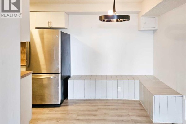 Kitchenette area with stainless steel refrigerator and a built-in bench seating, light wood flooring. - 14, 3726 Centre Street N, Calgary
