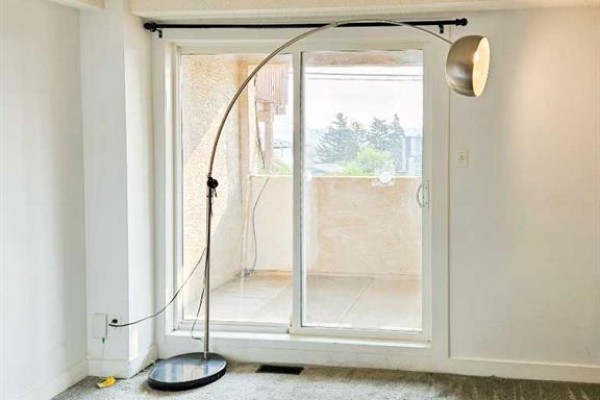 Living area with a large window, sliding glass door, and a floor lamp. - 14, 3726 Centre Street N, Calgary