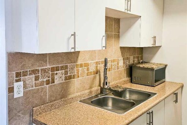 Close-up of a kitchen counter with a double sink, tiled backsplash, and white cabinetry. - 14, 3726 Centre Street N, Calgary