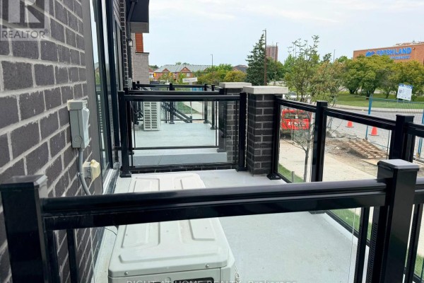 A balcony with glass railings overlooks a street with construction, featuring an outdoor air conditioning unit. - 14 - 10 Liben Way, Toronto