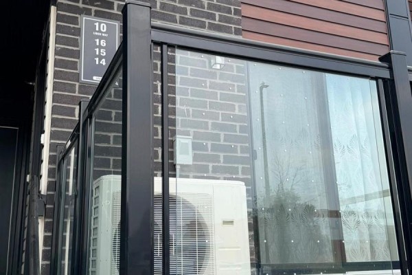 A balcony with a glass railing and an air conditioning unit on the exterior of a brick townhouse. - 14 - 10 Liben Way, Toronto