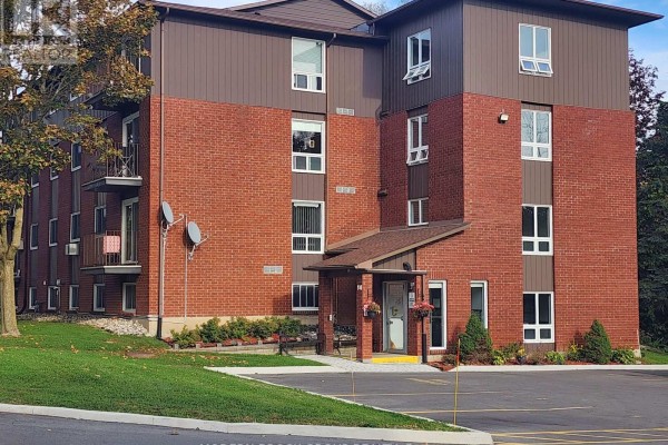 Exterior view of the brick apartment building with a paved parking lot and green lawn. - 14 - 14 Charlotte Place, Brockville