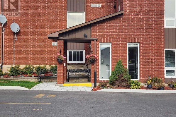 Close-up of the apartment building's brick entrance with a covered walkway and decorative plants. - 14 - 14 Charlotte Place, Brockville