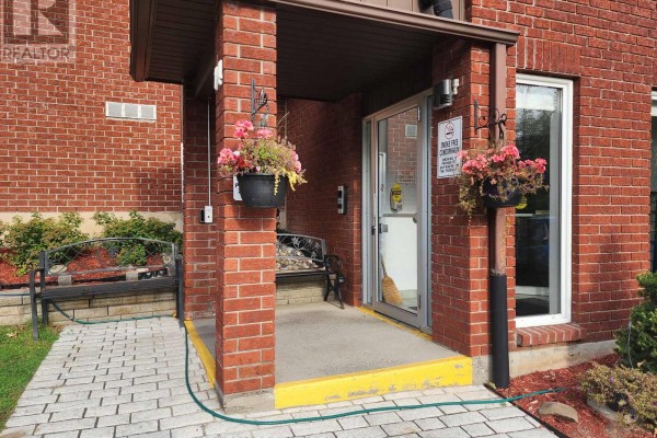 Entranceway to the apartment building with a brick facade, glass door, and hanging flower baskets. - 14 - 14 Charlotte Place, Brockville