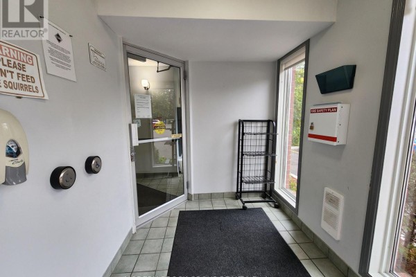 Interior view of the building's entrance lobby with tiled floors, a glass door, and safety notices. - 14 - 14 Charlotte Place, Brockville