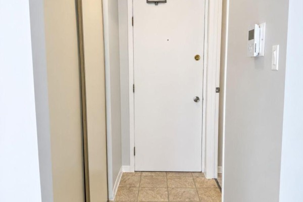 Hallway with a white front door, closet, and a wooden console table with decor. - 14 - 140 Laurier Street, Casselman