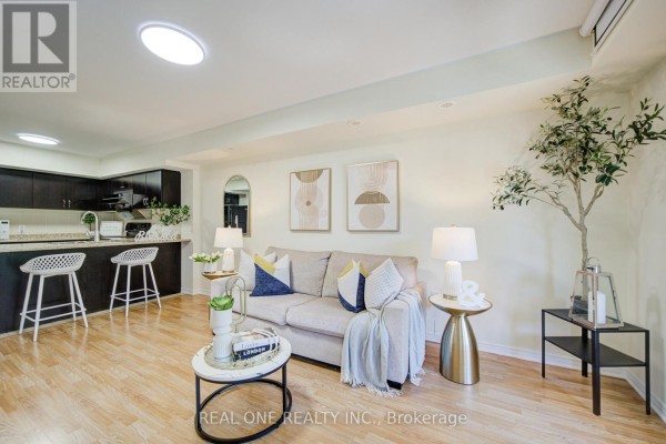 Bright living room with light wood floors, a beige sofa with blue and yellow pillows, and artwork on wall. - 14 - 2441 Greenwich Drive, Oakville