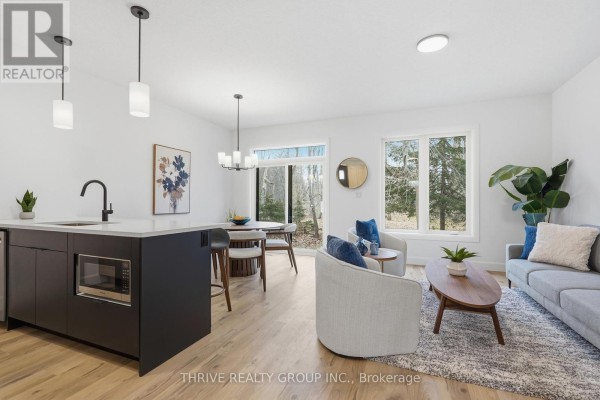 Open concept living and dining area with a kitchen island, gray sofa, and wood floors. - 14 - 279 Hill Street, Central Elgin