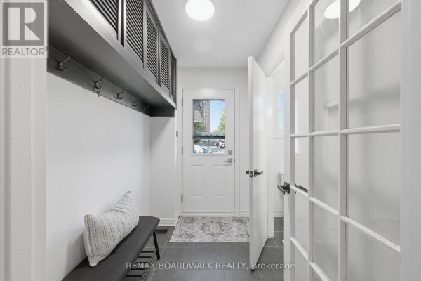 Bright entryway with white walls, dark gray floor tiles, bench, and storage. - 14 - 314 Stone Quarry Private, Ottawa