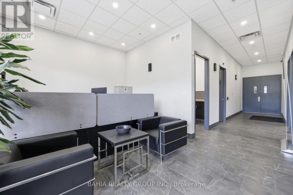 Interior reception area with grey flooring, black leather chairs, and desk. - 14 - 35 Stoffel Drive, Toronto