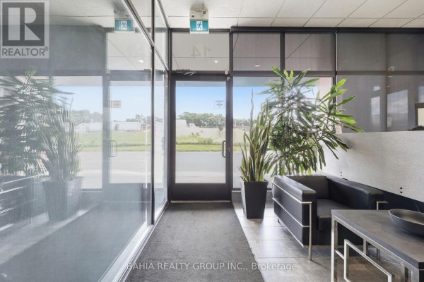View through glass doors to the outside, with plants and seating inside. - 14 - 35 Stoffel Drive, Toronto