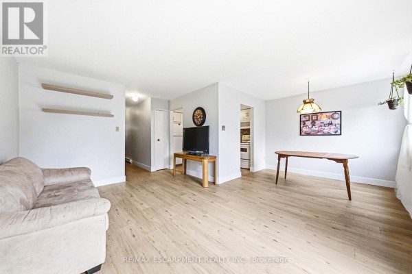 Living room with light wood laminate flooring, neutral walls, a beige sofa, and a dining table. - 14 - 564 Sheraton Road, Burlington