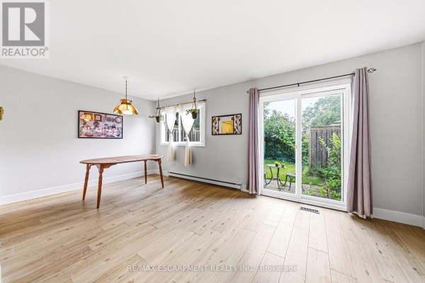 Dining area with light wood laminate flooring, neutral walls, a wooden table, and sliding glass doors to a backyard. - 14 - 564 Sheraton Road, Burlington