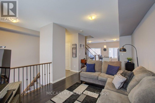 Living room with grey sofas, dark wood floors, railing, and view to the kitchen area. - 14 - 60 First Street, Orangeville