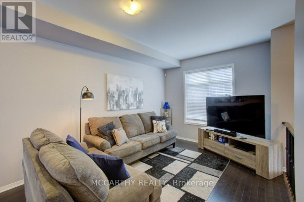 Living room with grey sofas, dark wood floors, television, and window with blinds. - 14 - 60 First Street, Orangeville