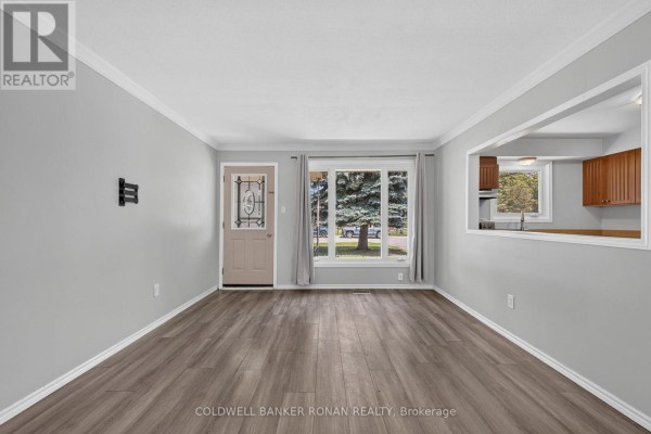 Living room with light grey walls, laminate flooring, a pass-through to the kitchen, and a view of the front yard. - 14 & 16 Fletcher Street, New Tecumseth