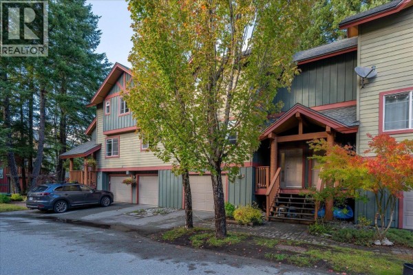 Exterior view of townhouse complex with green and tan siding, garage doors, and trees. - 14 1450 Vine Road Road, Pemberton