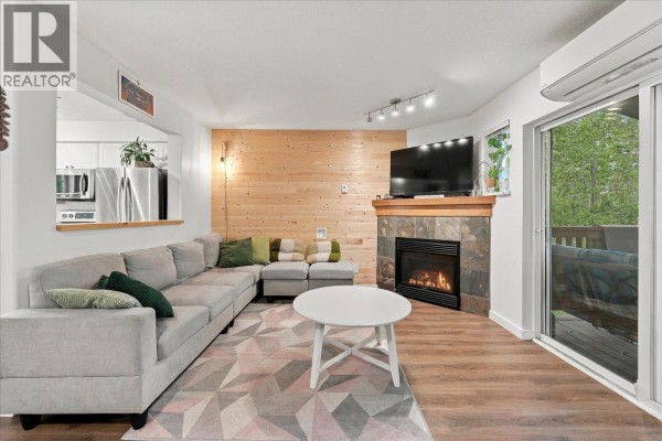 Living room with a grey sectional sofa, gas fireplace, wood accent wall, and white coffee table. - 14 1450 Vine Road Road, Pemberton