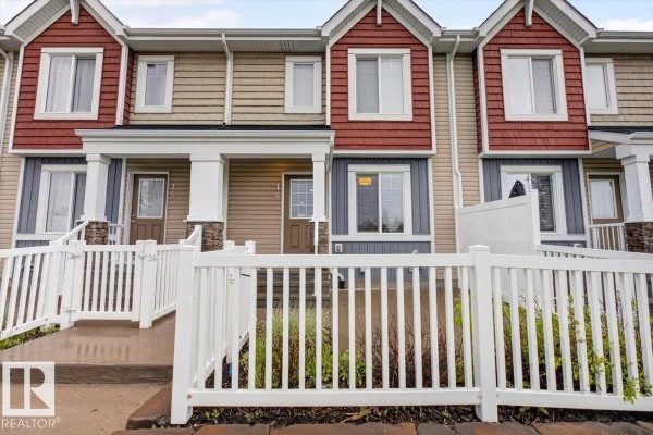 Front entrance view of townhouse units with porches, white fences, and stone accents. - #14 1508 105 St Nw, Edmonton