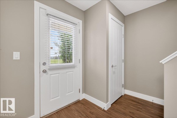 Interior view of a townhouse entryway with a white door, window, and wood-look flooring. - #14 1508 105 St Nw, Edmonton