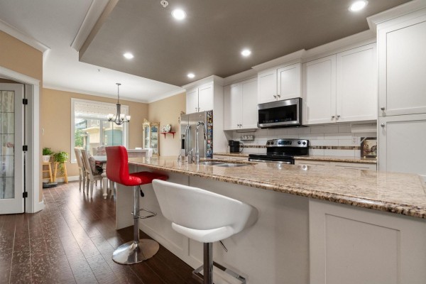 Kitchen with white cabinets, granite counters, and stainless steel appliances, facing the dining area. - 14 45290 Soowahlie Crescent, Garrison Crossing, Chilliwack