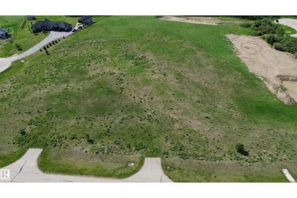 Aerial view of a large, undeveloped grassy lot with neighboring houses and a pond. - #14 53524 Rge Road 275, Rural Parkland County