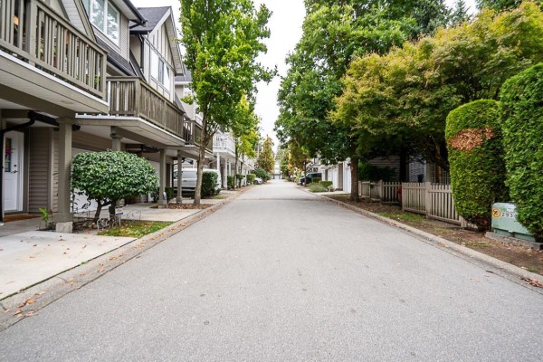 Street view of a townhouse complex with garages and balconies, lined with trees. - 14 8775 161 Street, Surrey